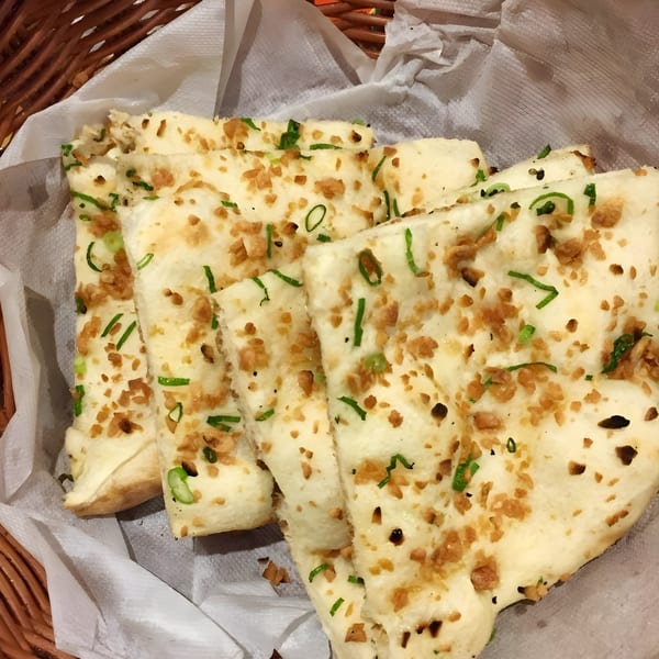 Garlic naan bread with green onions and crispy garlic bits, served in a basket with white paper.