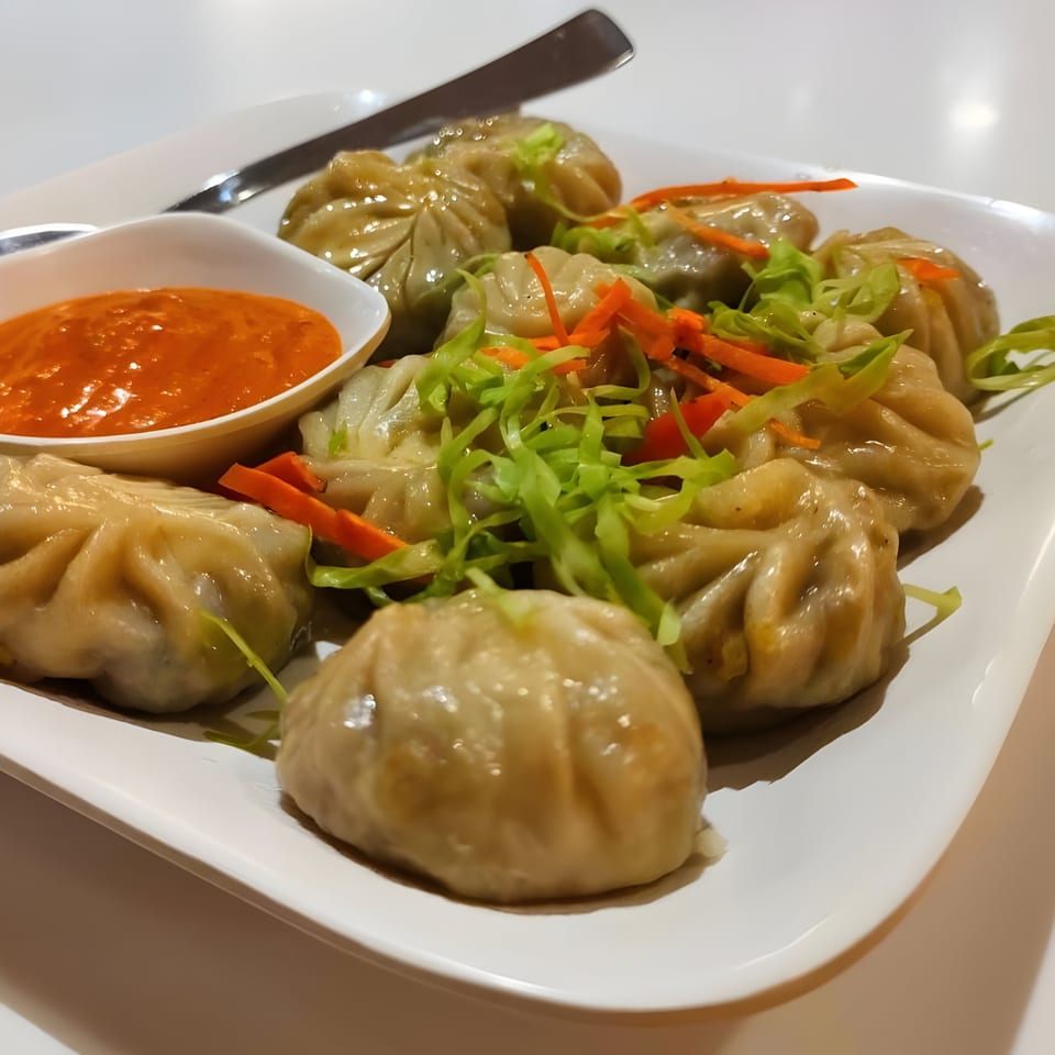 A plate of steamed momos, garnished with shredded cabbage and carrots, served with a red dipping sauce.