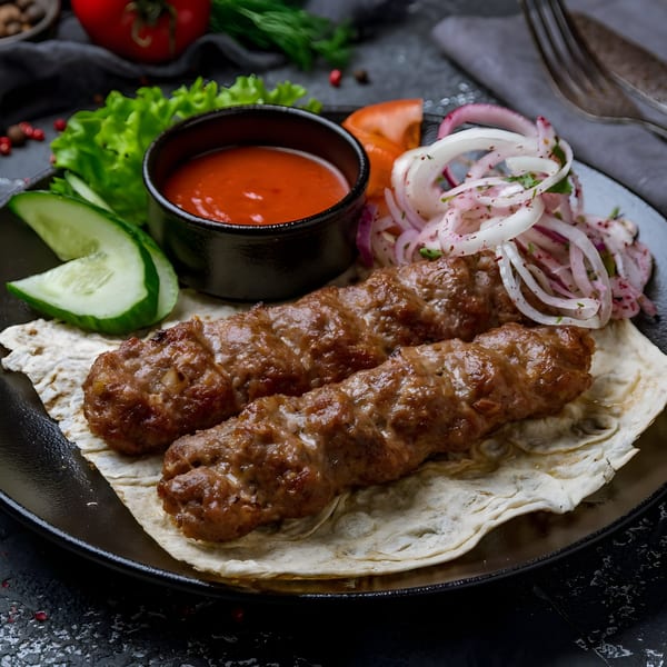 Two Indian spice kebabs on flatbread with red sauce, sliced cucumbers, and pickled onions.
