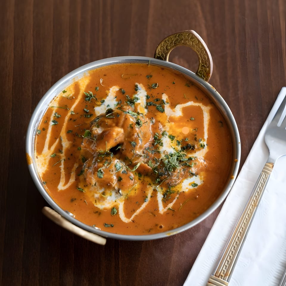 Butter chicken in a traditional Indian serving bowl, garnished with cream and herbs, on a wooden table.