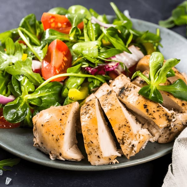 Grilled chicken breast slices with a fresh green salad on a gray plate, ready to be served.